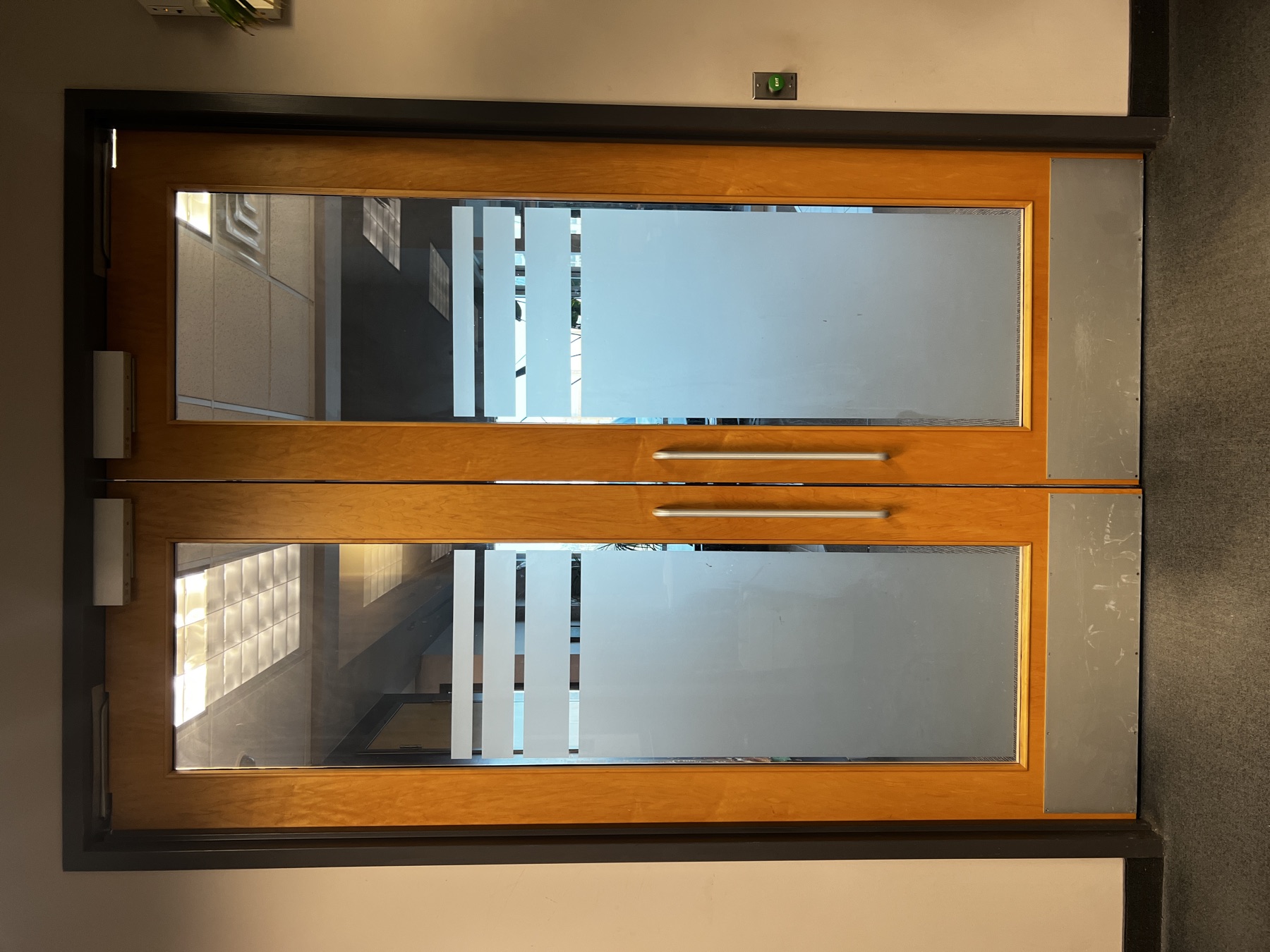 Commercial wood-and-glass doors with closers and an exit indicator.