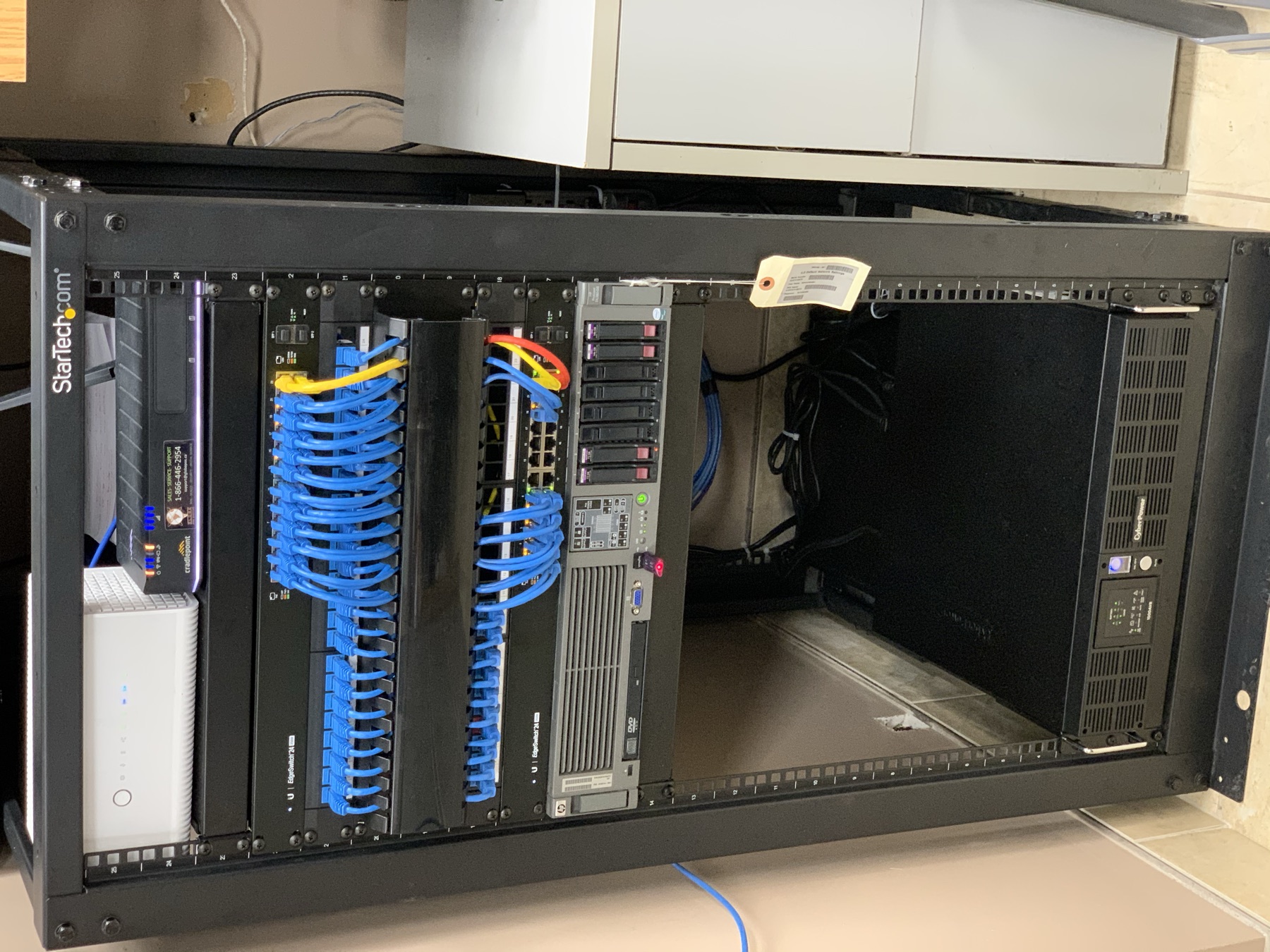 Full-height rack with blue patching, switch, and a rack UPS.