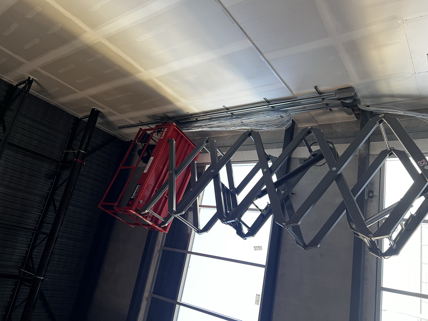 Scissor lift at height with a vertical cable bundle on a tall wall.