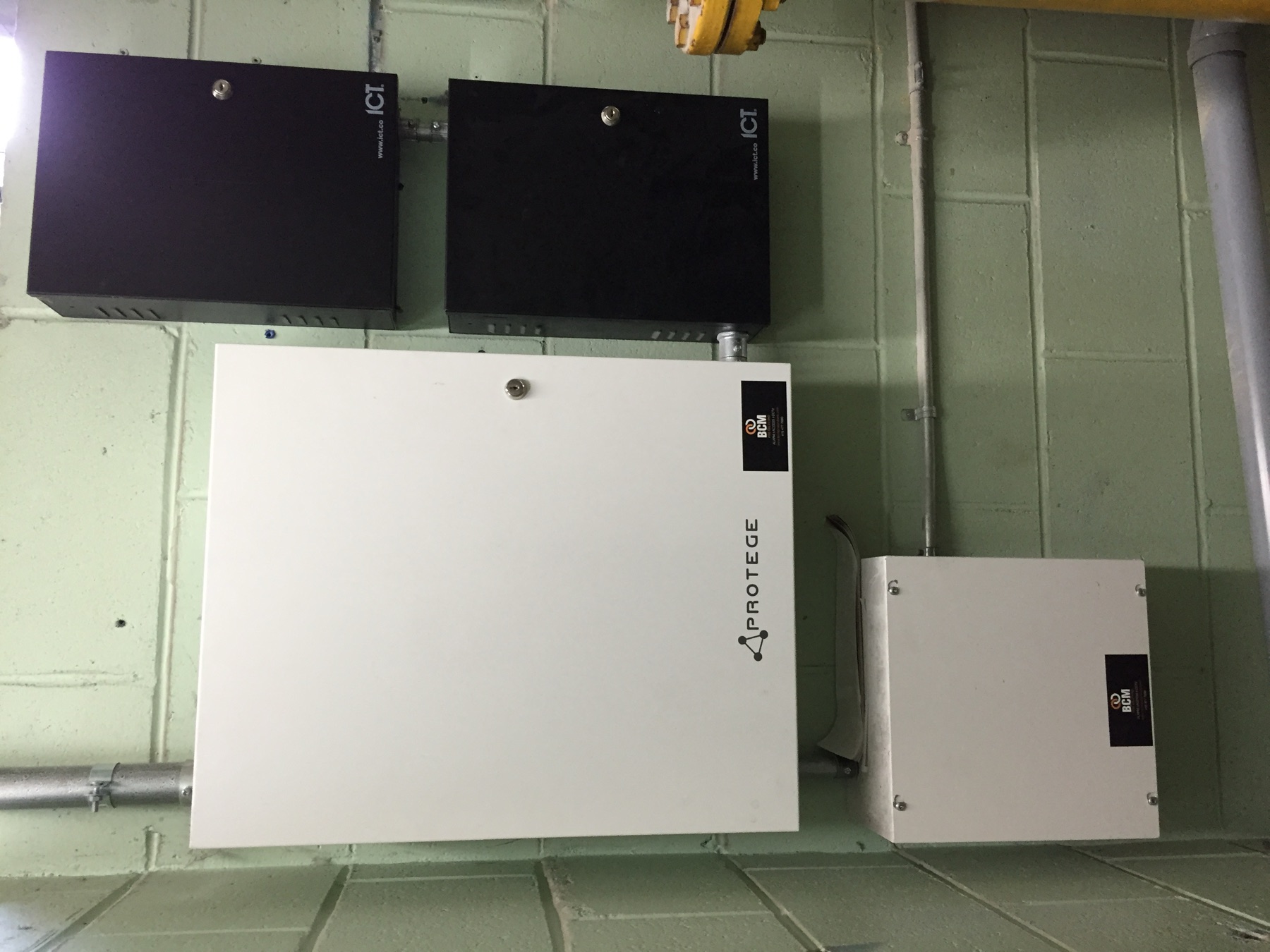 Protege and ICT enclosures with BCM plates on a cinder-block wall.