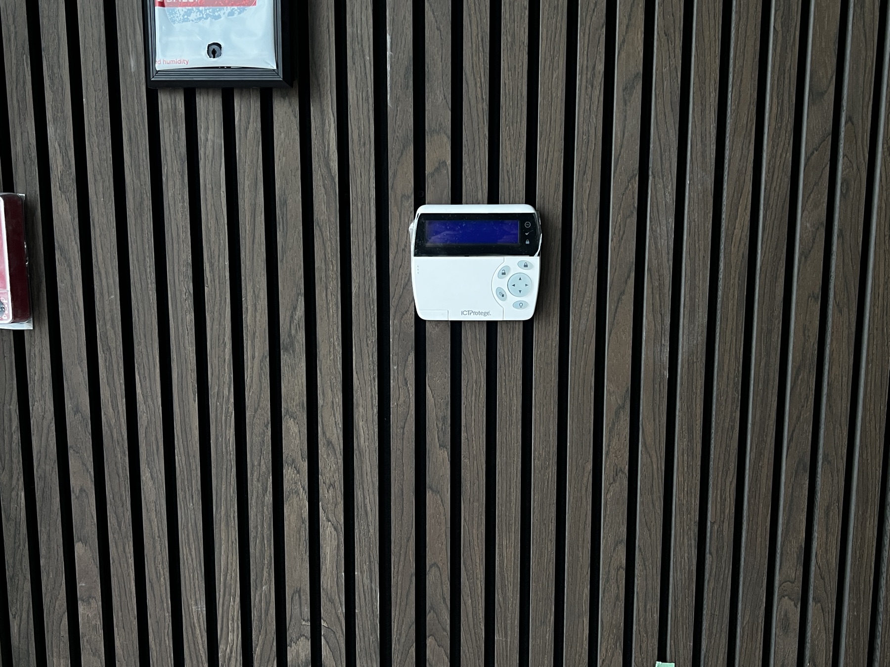 ICT Protege keypad on a dark wood-slat wall.